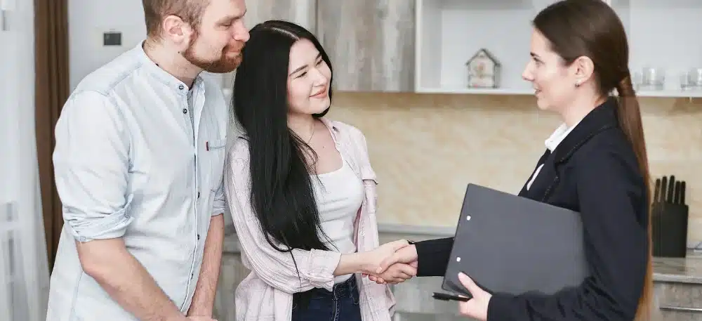 15 Proven Ways to Get Listings as a Real Estate Agent (& Keep Them Coming) 5 A happy couple shaking hands with a real estate agent, indicative of client satisfaction with commission rates