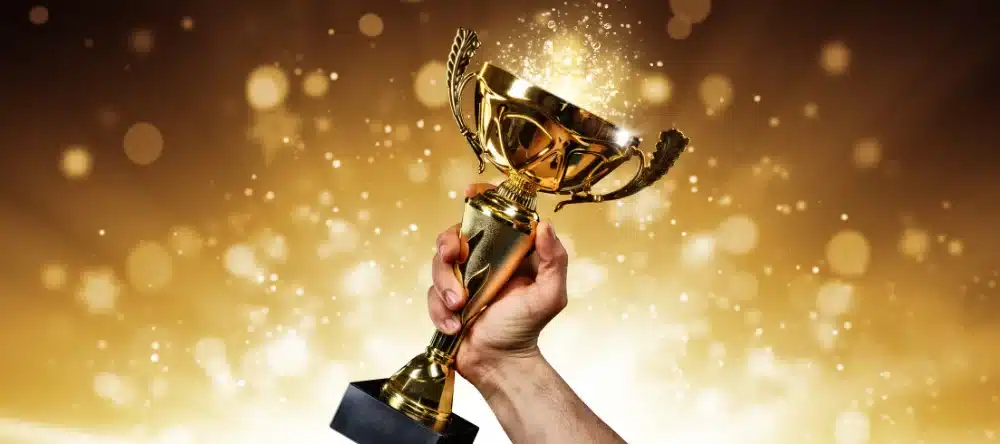 Agents, Repurpose Content for BIG Results 2 Hand holding a trophy against a golden bokeh background, symbolizing success for real estate agents during a recession.