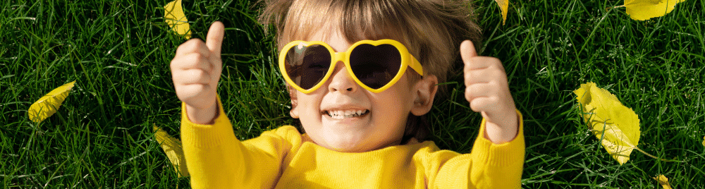 eXp Realty Healthcare: Save Up to 80% on Premium Care! 2 Unlock the Perks - Why eXp Realty Healthcare Rocks. A child wearing heart shaped sunglasses lying in grass